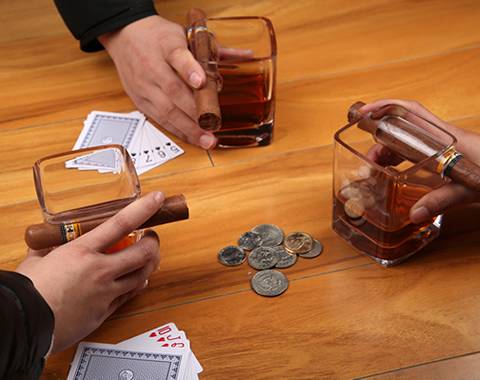 Three people are playing the poker on the desk, and each of them is catching a cigar whiskey glass cup.