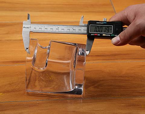 A hand is measuring the height of the cup which placed on the desk.