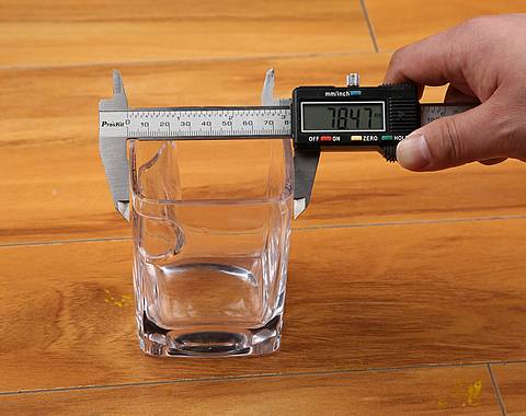 A hand is measuring the length of the cup which placed on the desk.