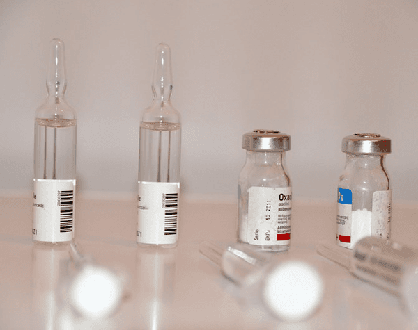 La imagen muestra cuatro botellas de viales de vidrio farmacéutico con medicamentos líquidos.