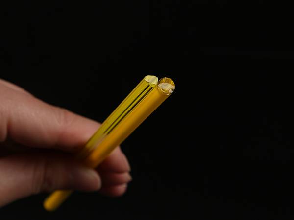 Un tube jaune prismatique et un tube capillaire jaune rond sont en main sur fond noir.